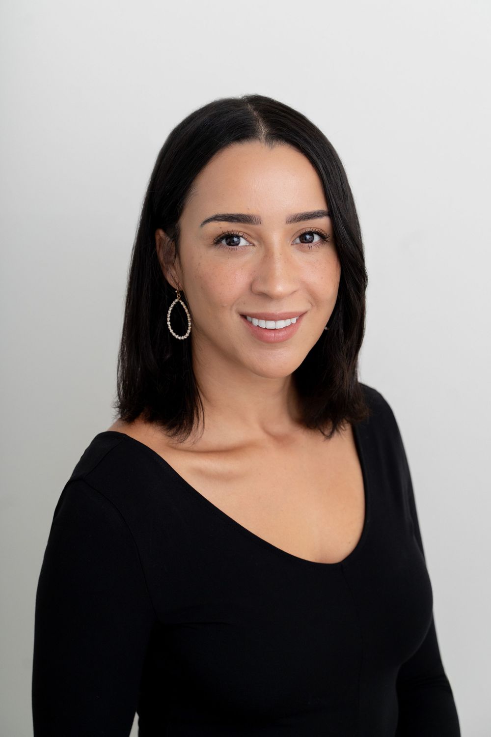 Professional headshot of a smiling woman with dark hair wearing a black top and teardrop earrings.