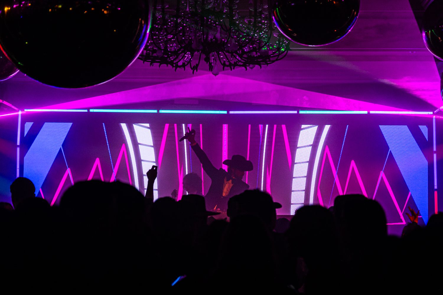 Silhouetted crowd watches performers on stage under dramatic purple and blue lighting at a concert venue.