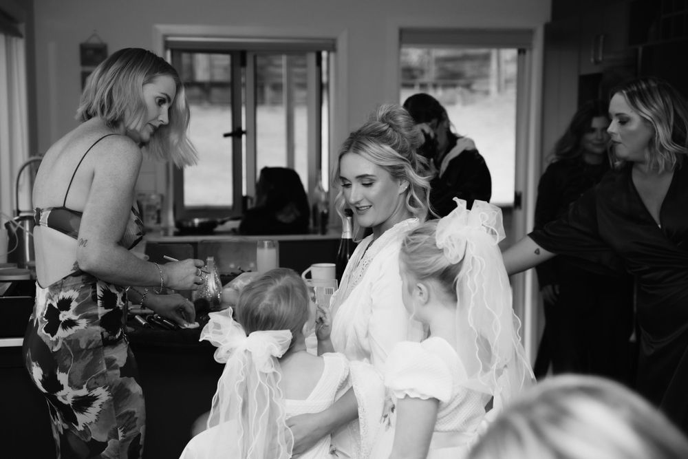 A candid black and white moment during wedding preparations with attendants helping.