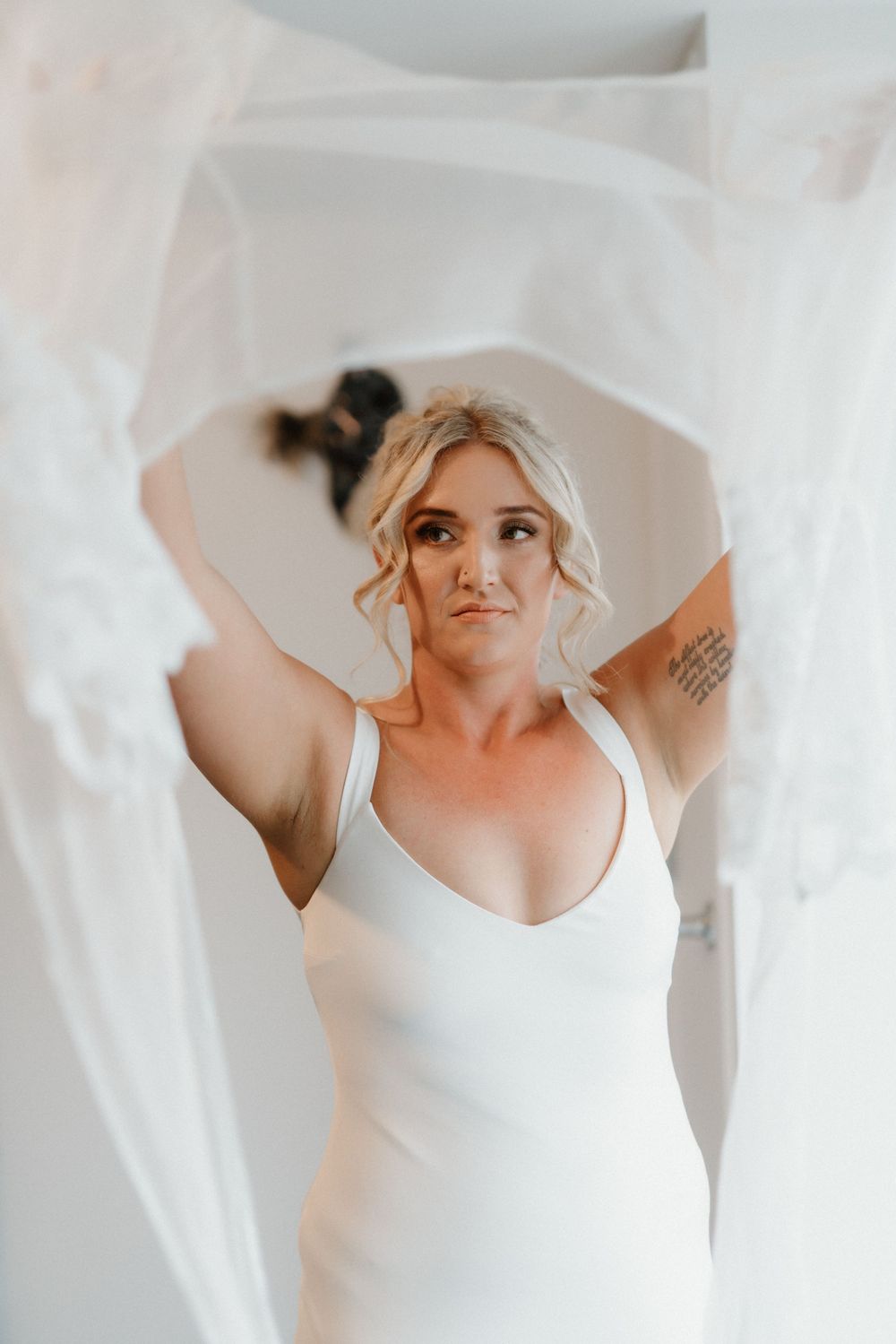 An ethereal bridal portrait framed by flowing white fabric in soft natural light.