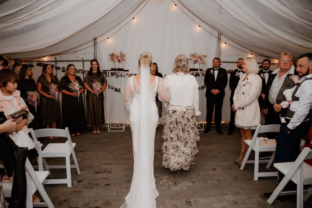 Wedding processional in white tent with draped fabric ceiling and photo displays along the walls.