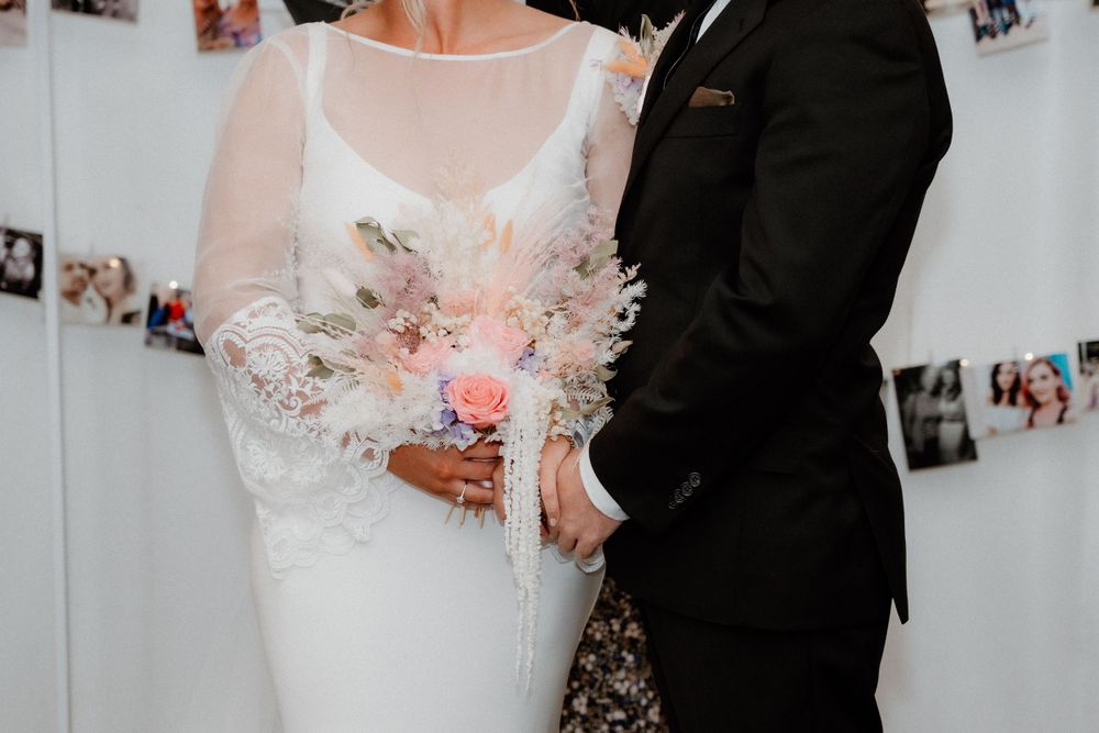 Close-up of couple holding delicate pink and white bouquet during wedding ceremony.