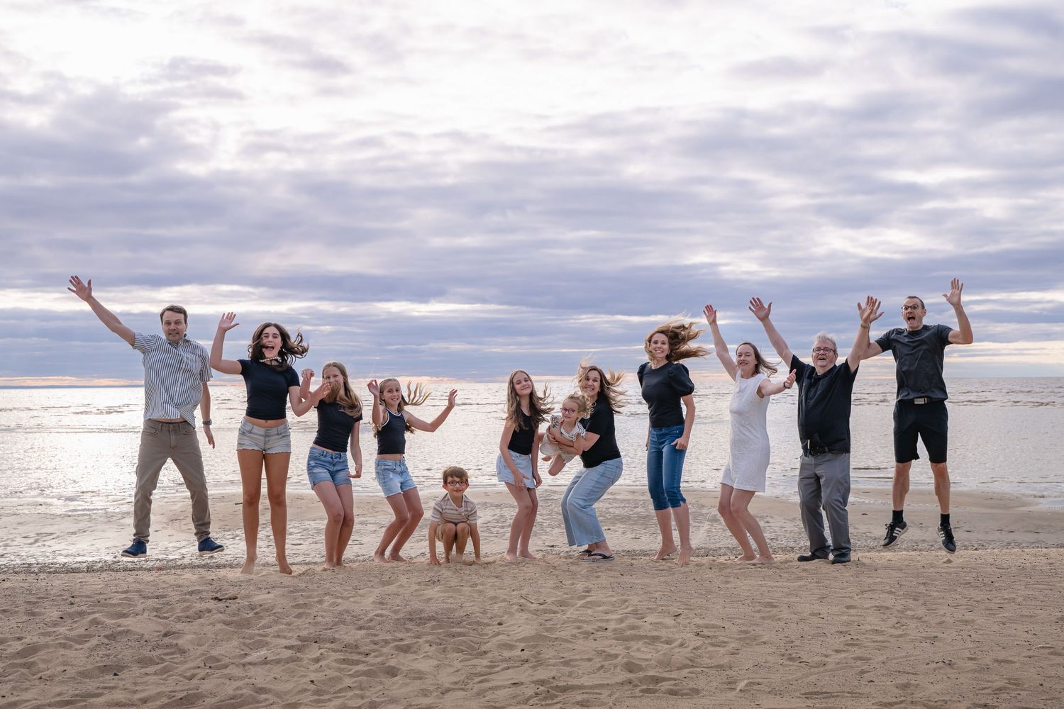 Famille heureuse sautant dans les airs à la plage de Saint-Gédéon sous un ciel nuageux mauve et bleu