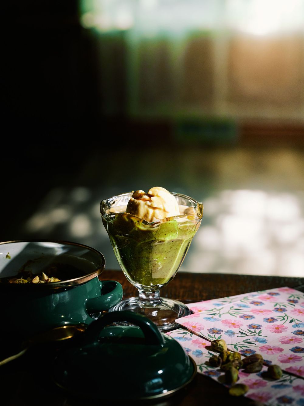 A close-up of green sliced avocado arranged on a blue plate against a pink floral tablecloth in moody lighting.