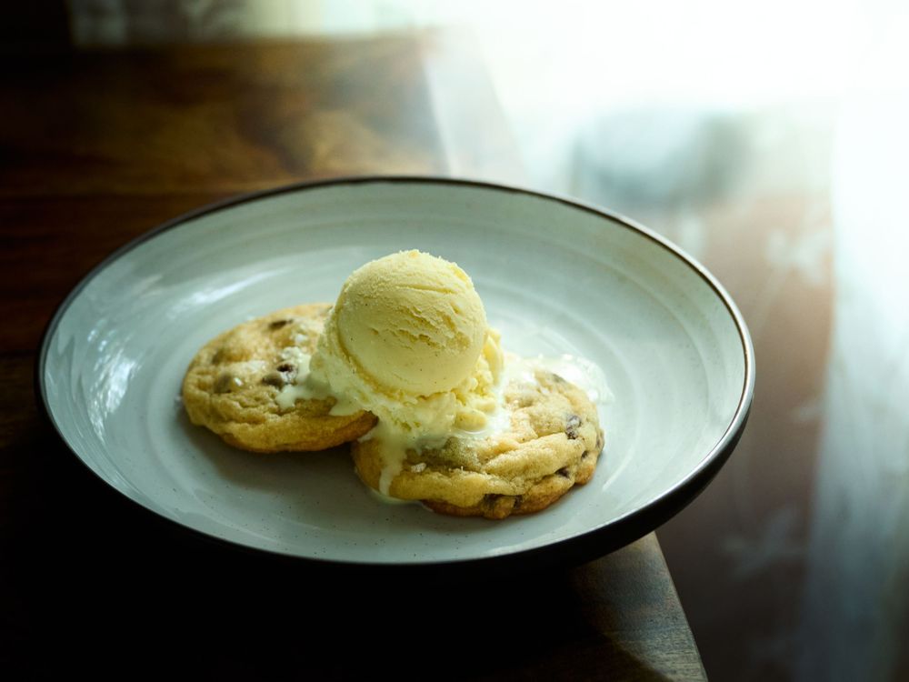 Fresh baked chocolate chip cookies with melting vanilla ice cream on white plates against a dark background.