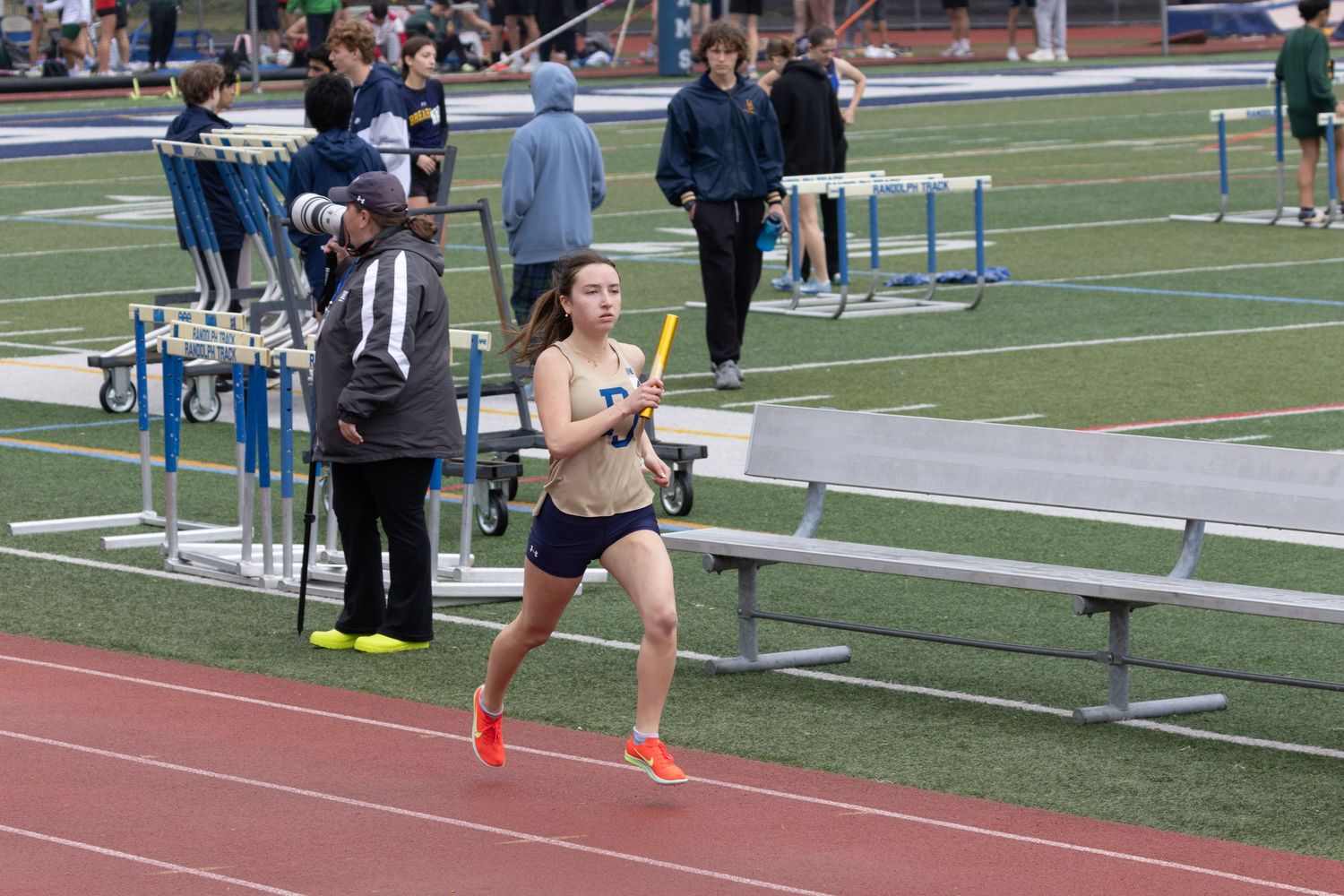 A female athlete runs a relay race on an outdoor track holding a yellow baton.