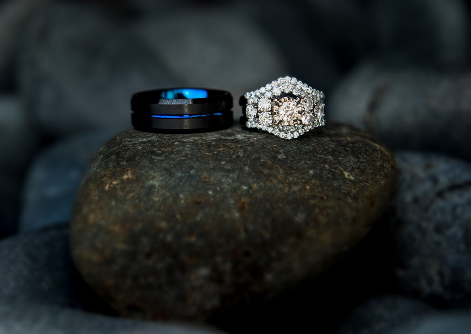 Wedding rings displayed on dark stone - blue tungsten band and diamond engagement ring.