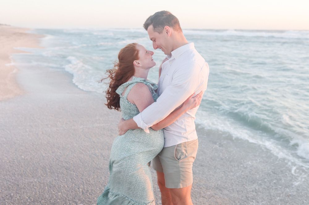 A romantic couple embraces on a beach at sunset while waves crash along the shoreline.