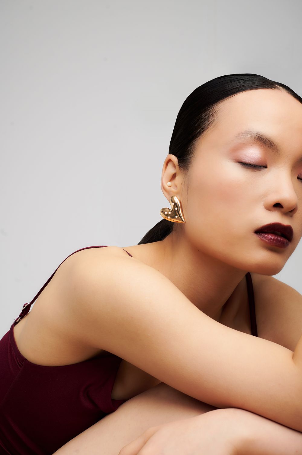 Artistic beauty portrait with burgundy lipstick and gold earrings against grey background.