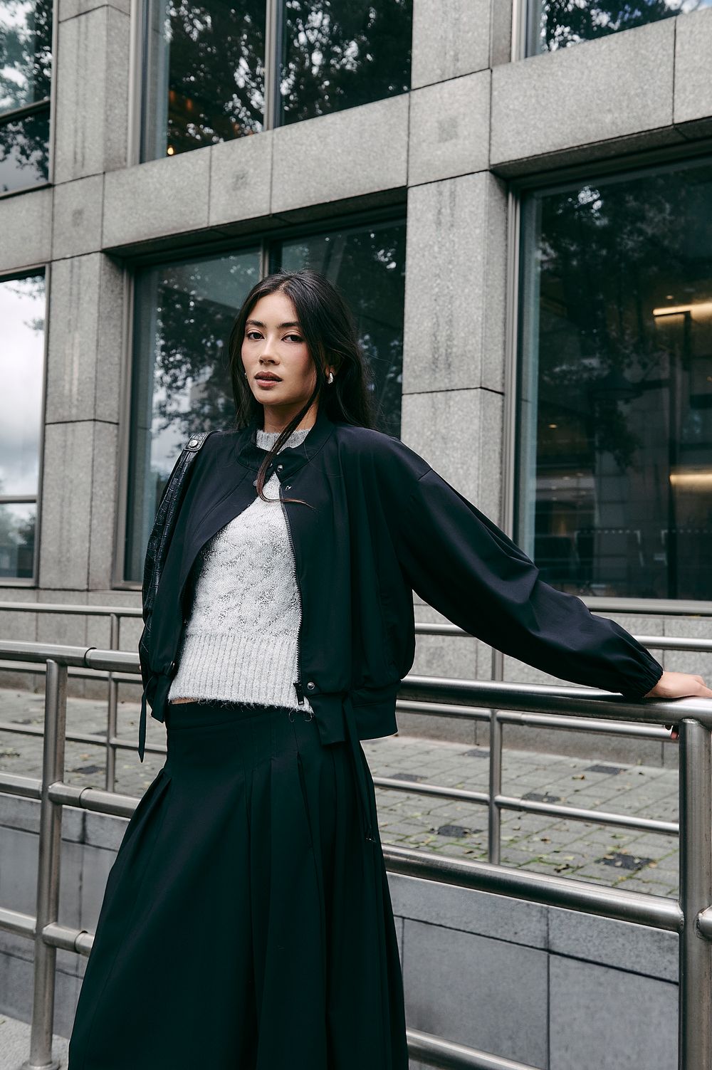 A person in a black coat strikes dynamic poses against a modern building's glass windows and concrete exterior.