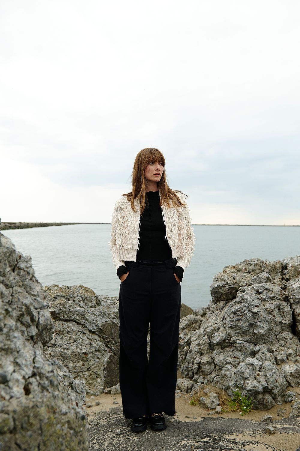 A series of artistic photos showing a person in black clothing sitting on rocky coastal terrain against an overcast sky.