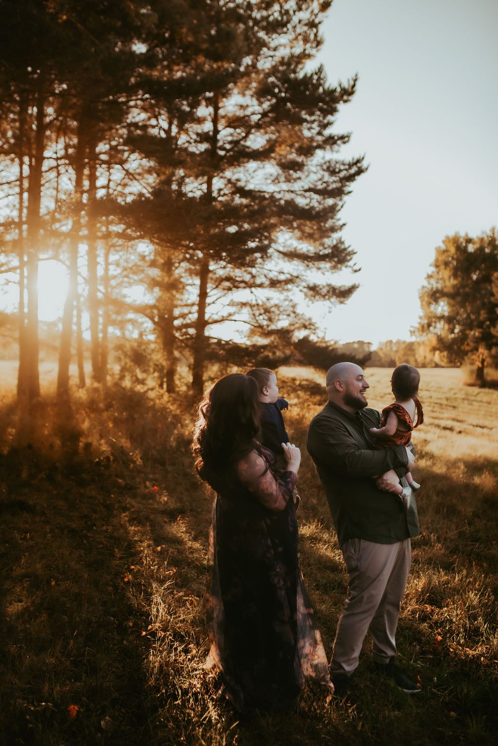 Family silhouettes embrace in a warm sunset glow among tall pine trees on a hillside, family photos