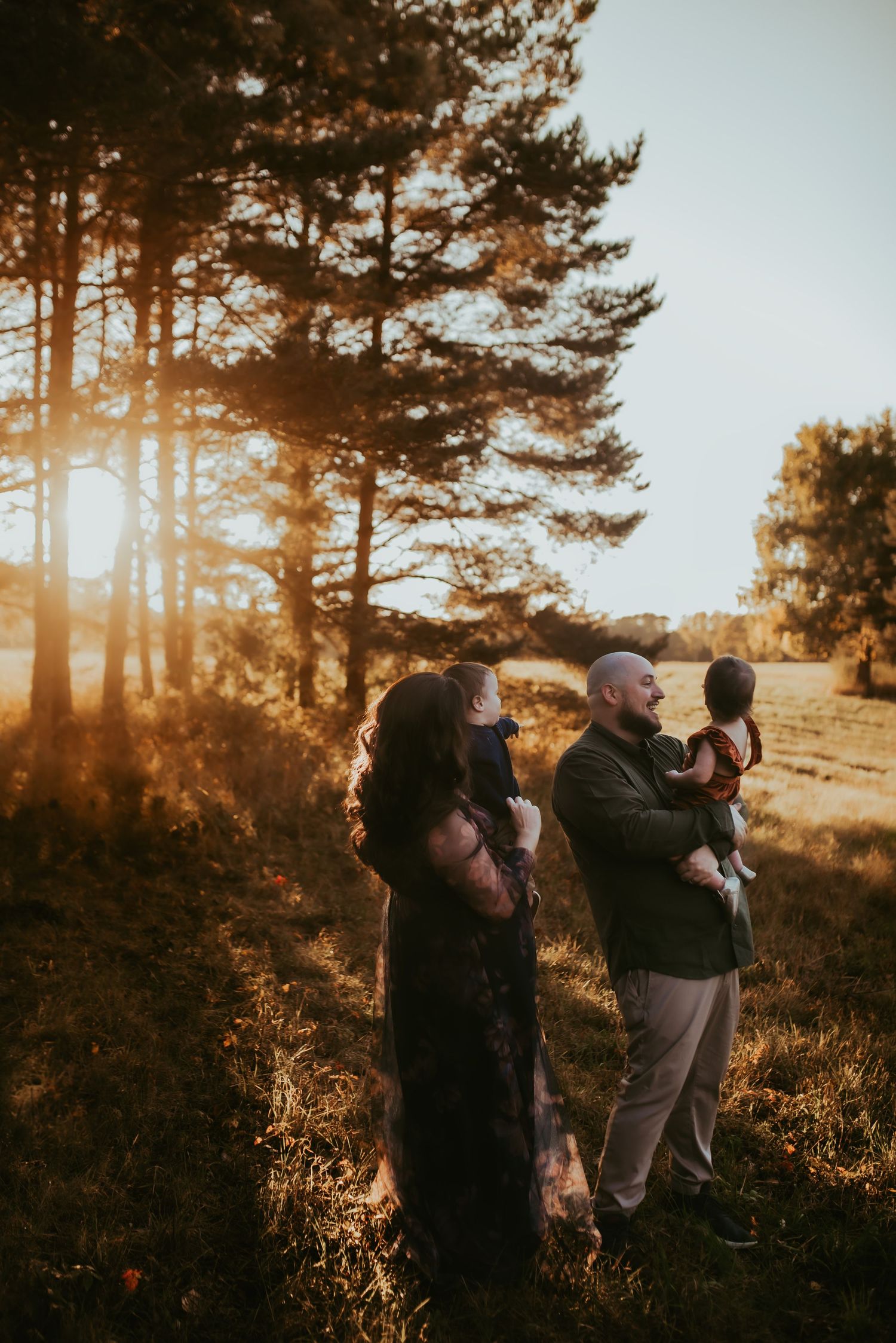 Family silhouettes embrace in a warm sunset glow among tall pine trees on a hillside, family photos