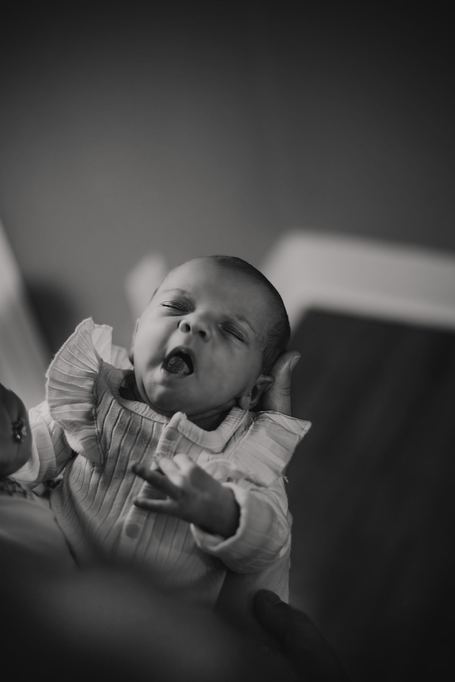 A yawning baby in a ruffled white shirt captured in black and white photography.
