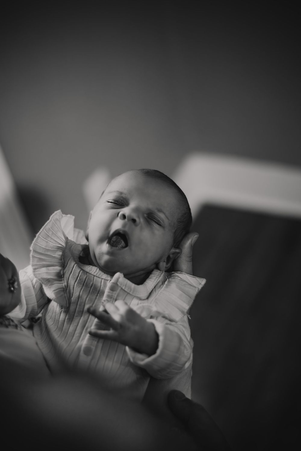 A yawning baby in a ruffled white shirt captured in black and white photography.