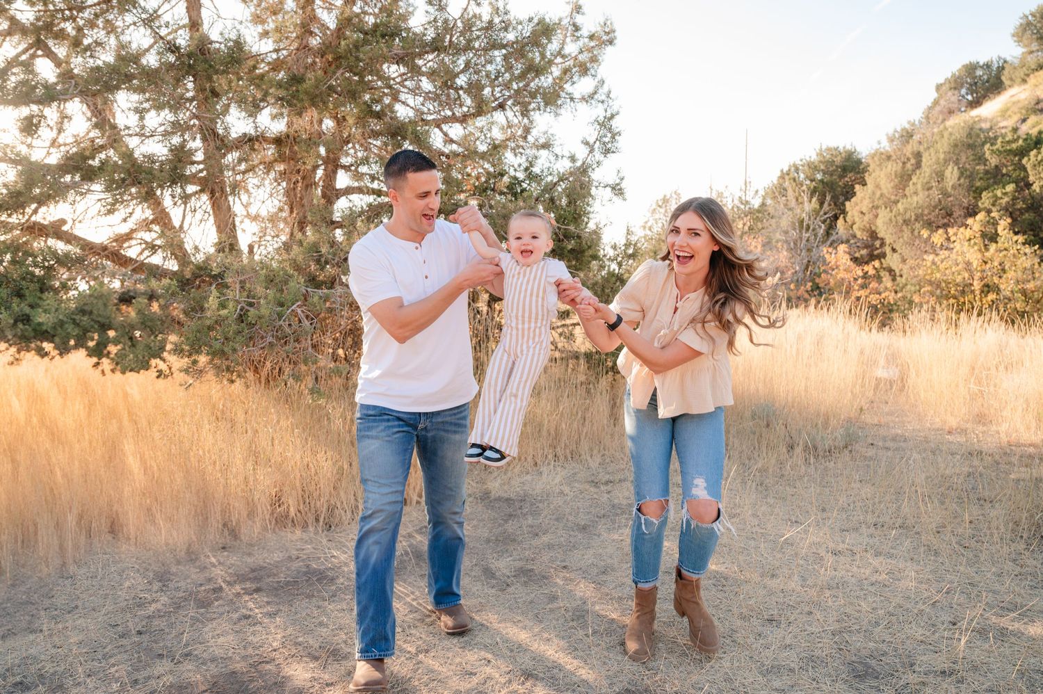 Family playing and laughing together in golden field at sunset.