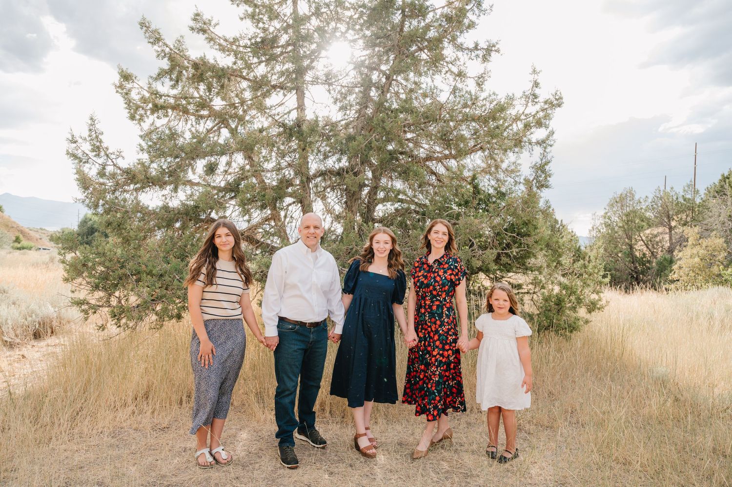 Family portrait under large tree in rustic mountain meadow setting.