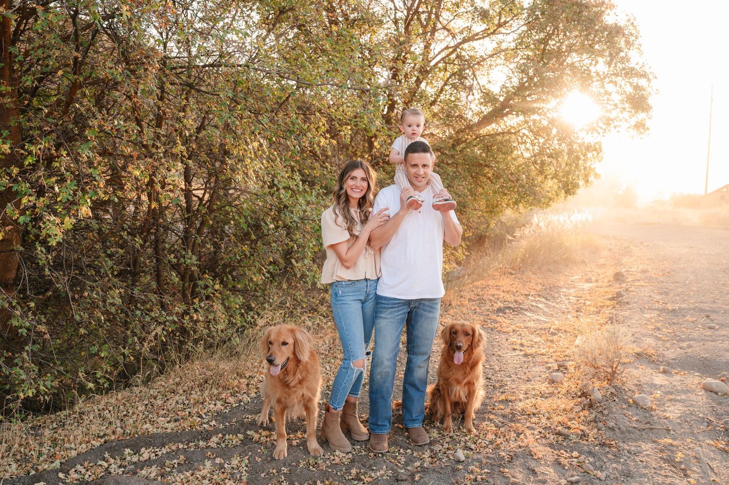 Couple walking dogs on trail during golden hour with sunburst through trees.