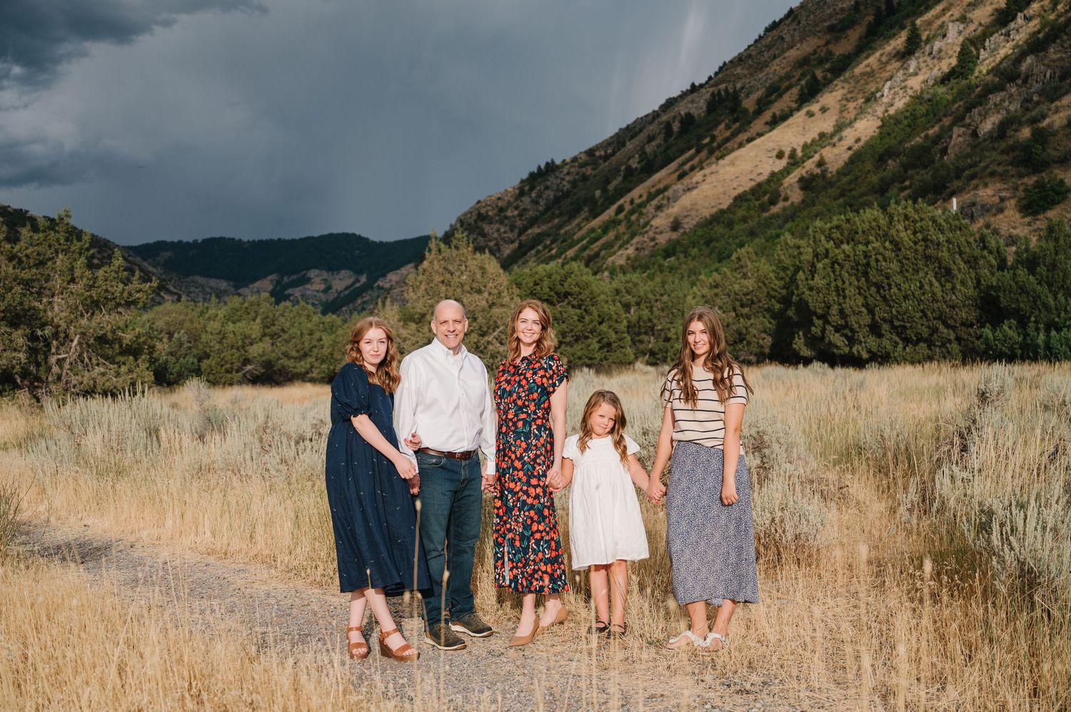 Family group posed in golden field with dramatic mountain backdrop.