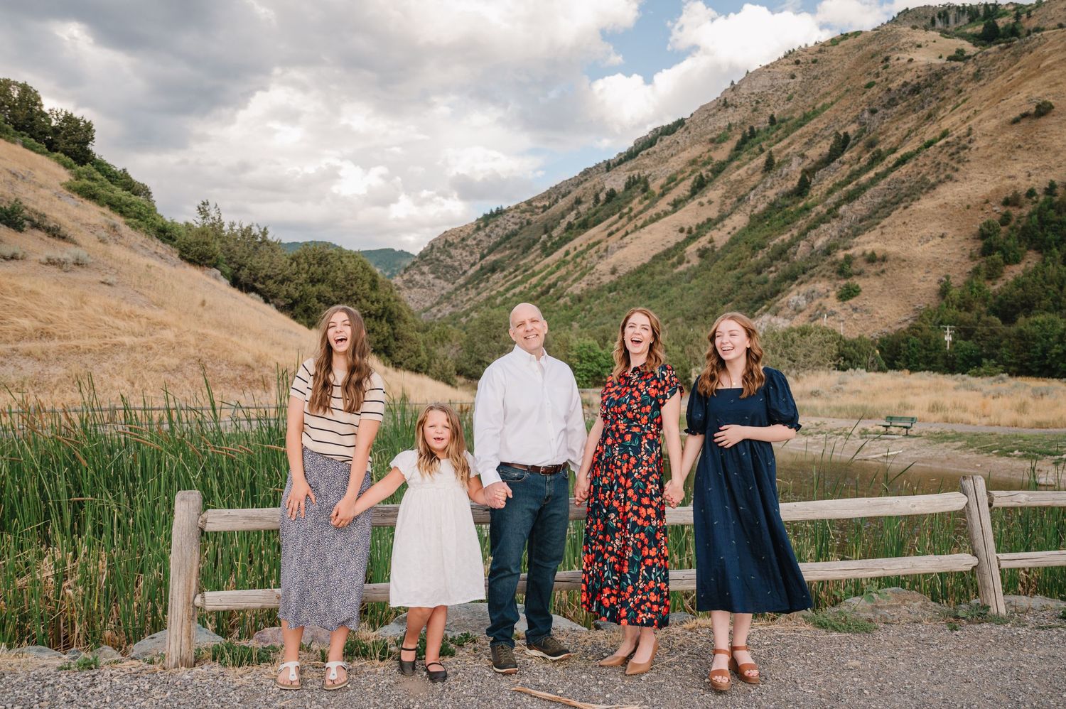 Family group posed by wooden fence in mountain valley with dramatic cloudy sky.