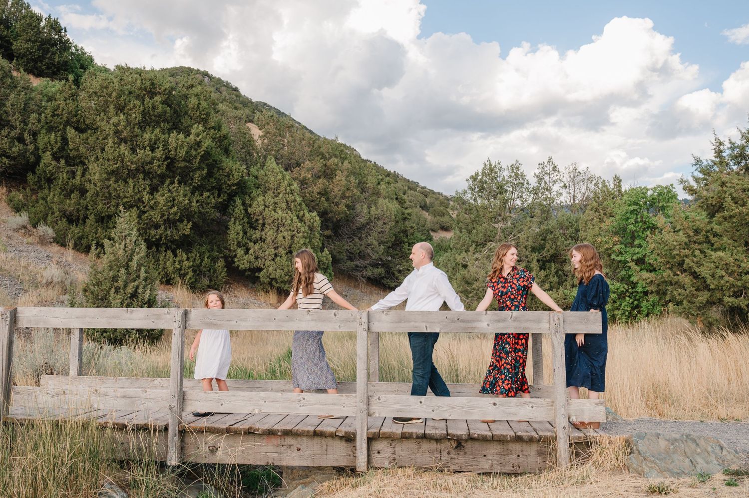 A group stands together on a wooden boardwalk surrounded by natural grassland and mountains.