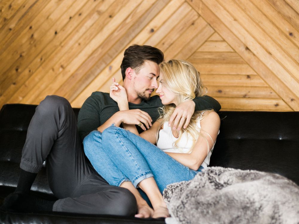 A couple laughs together while relaxing on a couch in a room with wooden walls.