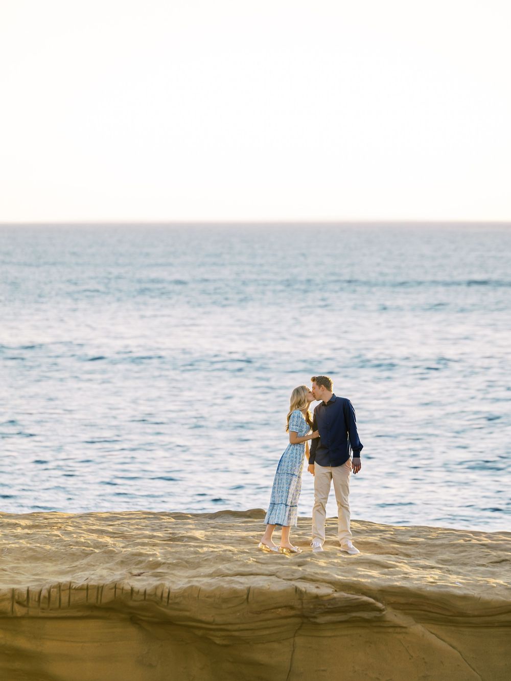 A couple walks along the sandy beach at sunset with ocean waves in the background.