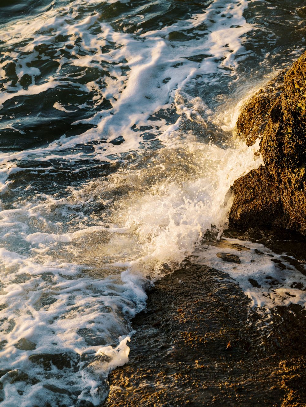 Ocean waves crash against rocky coastal cliffs creating dramatic white foam splashes.