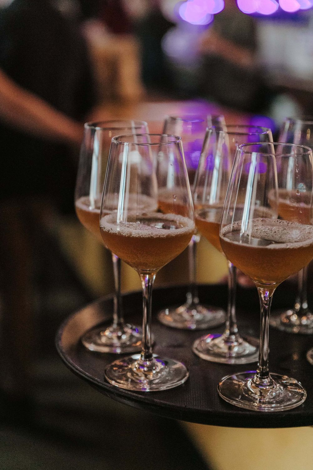 Wine glasses filled with rose-colored drinks on a serving tray with purple ambient lighting in the background.