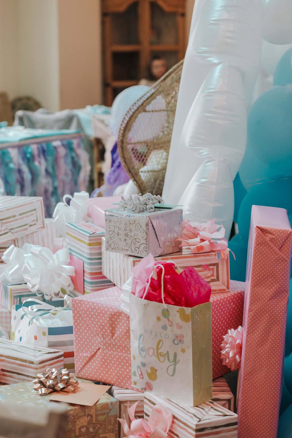 A collection of baby shower gifts wrapped in pastel pink and blue papers with bows and ribbons arranged on a table.