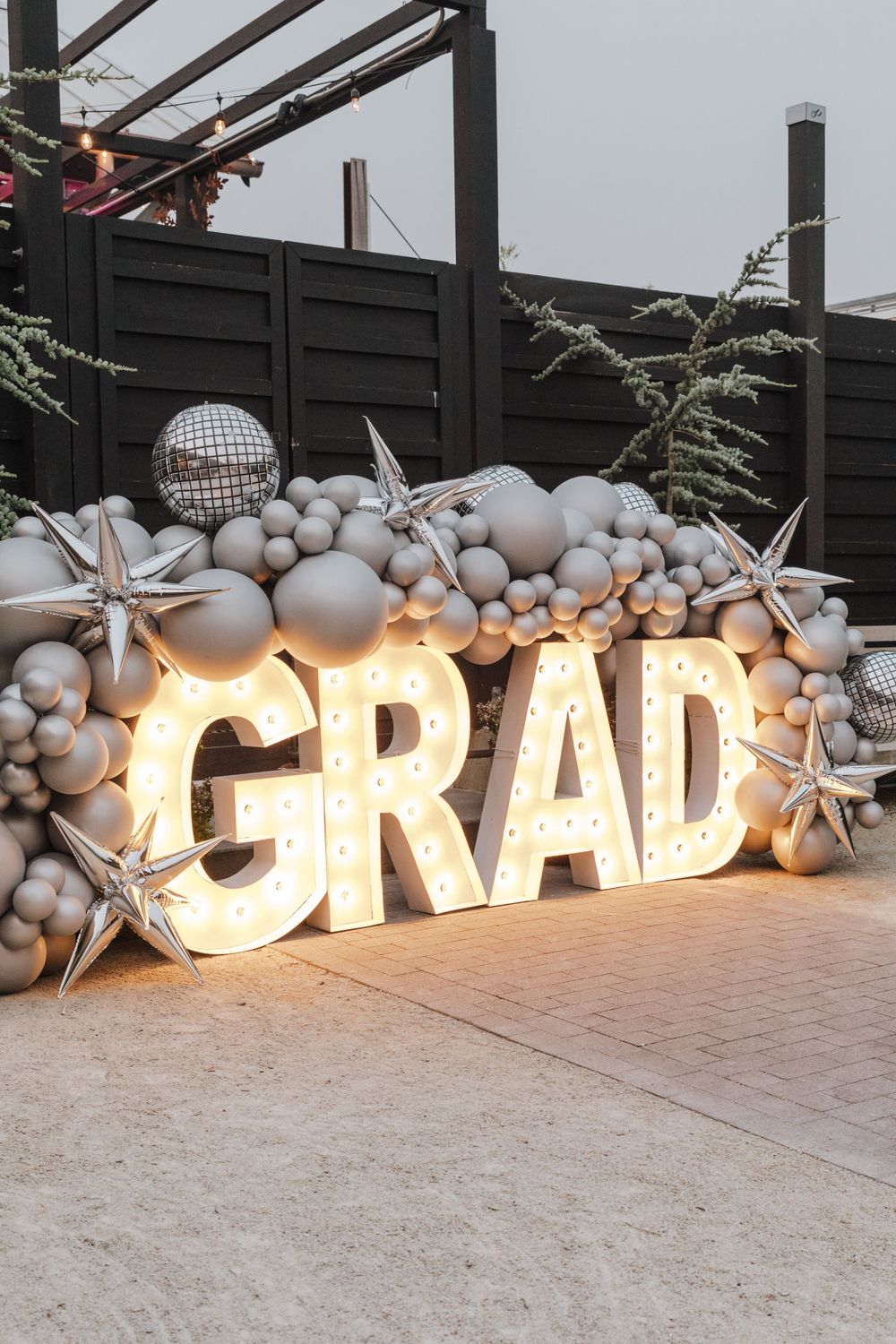 Illuminated GRAD marquee letters with silver balloon arch, disco ball, and starfish decorations against dark fence.