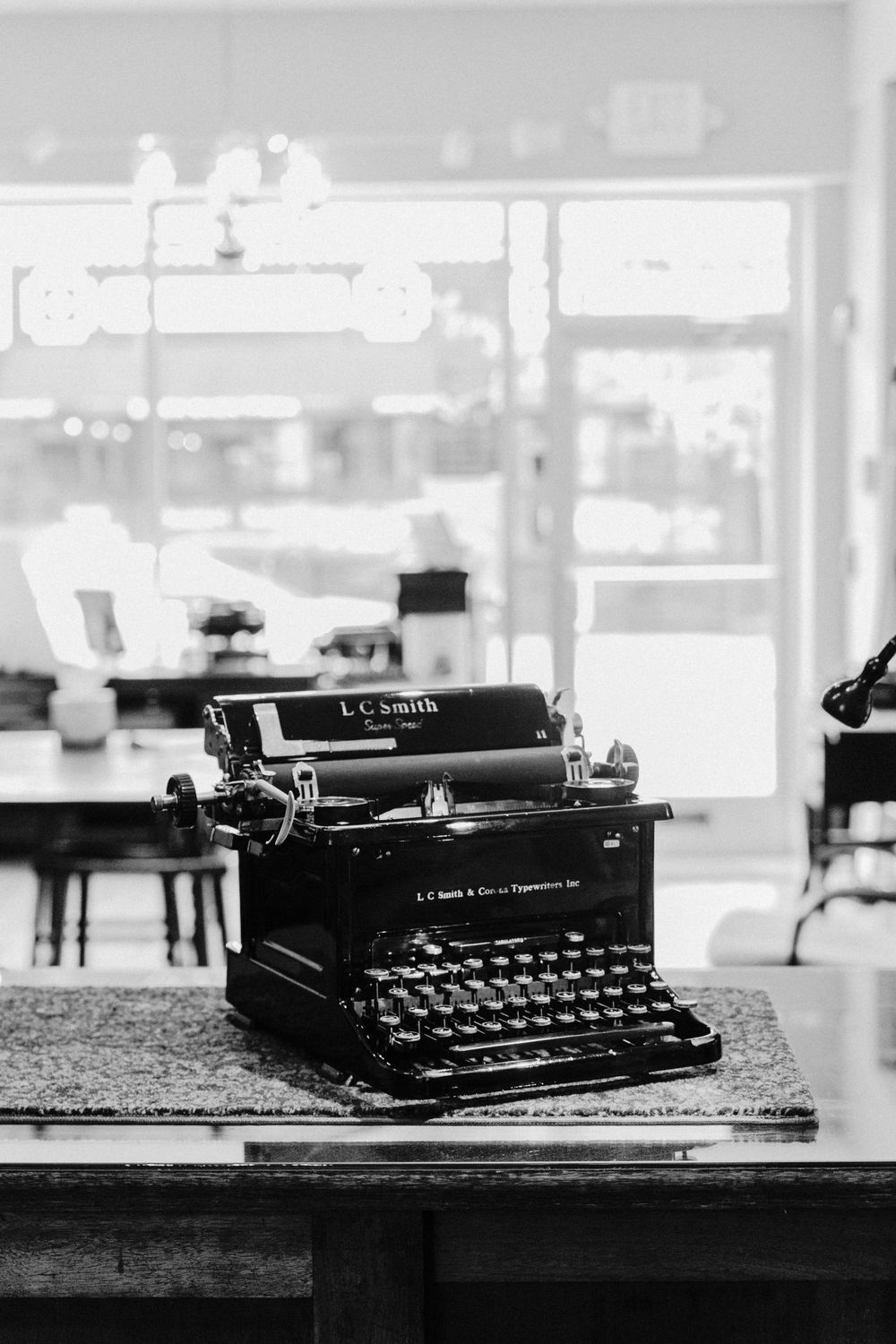 Vintage black LC Smith typewriter sits on wooden table in black and white photograph.