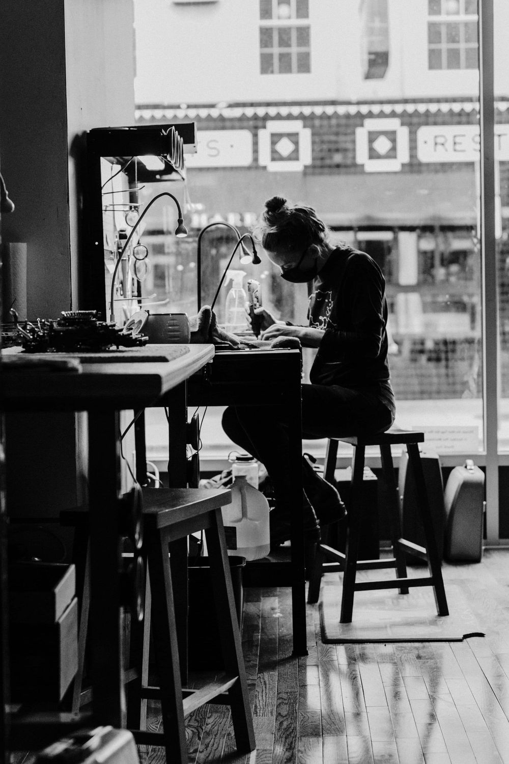 A silhouette of a person working at a laptop in a cafe window seat creates a moody black and white composition.
