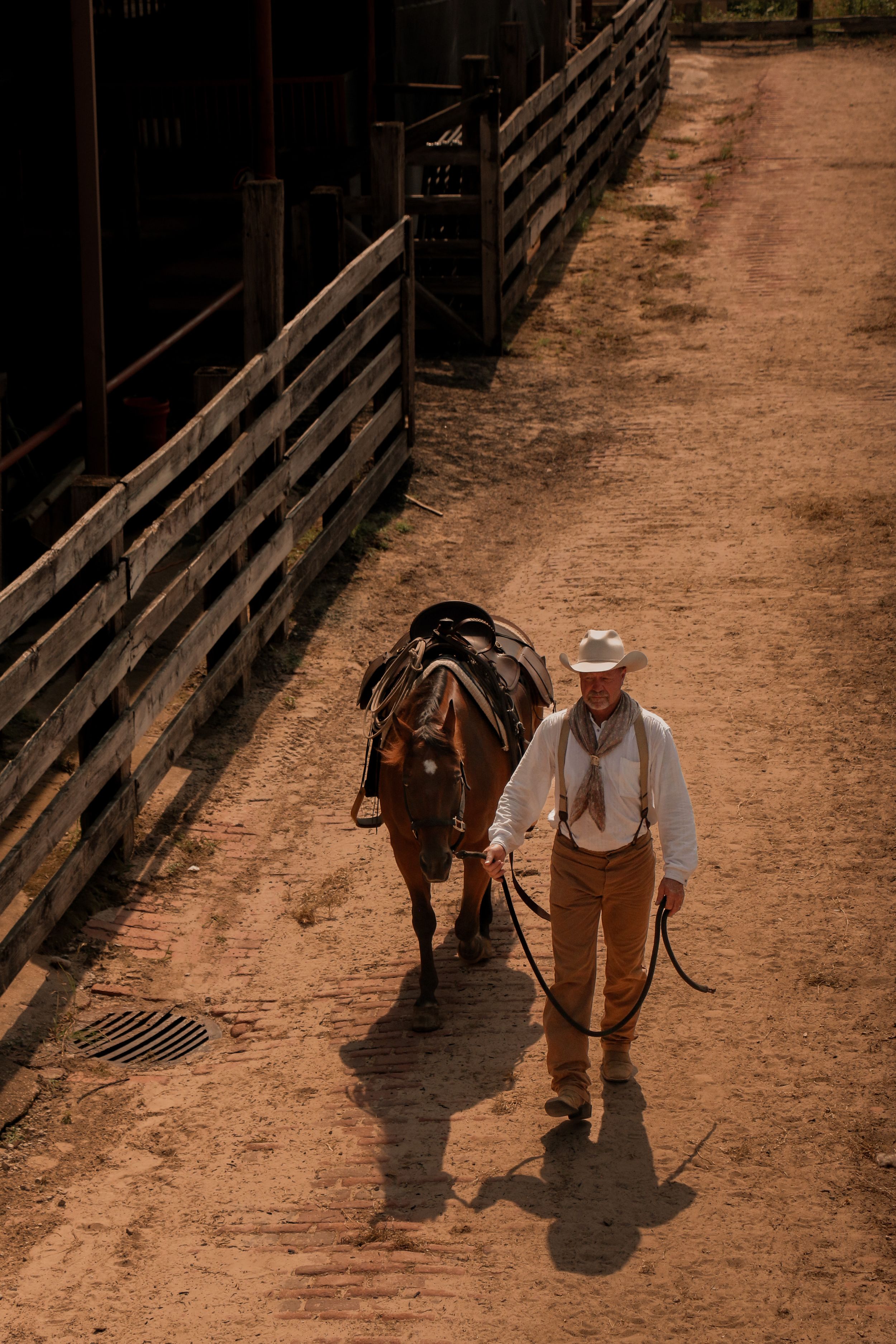 Person leading a horse through a wooden-fenced corridor at a historic stockyard.