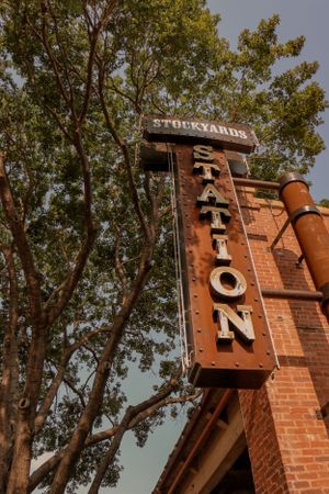 Vintage 'Station' sign on brick building with trees in background at Fort Worth Stockyards.