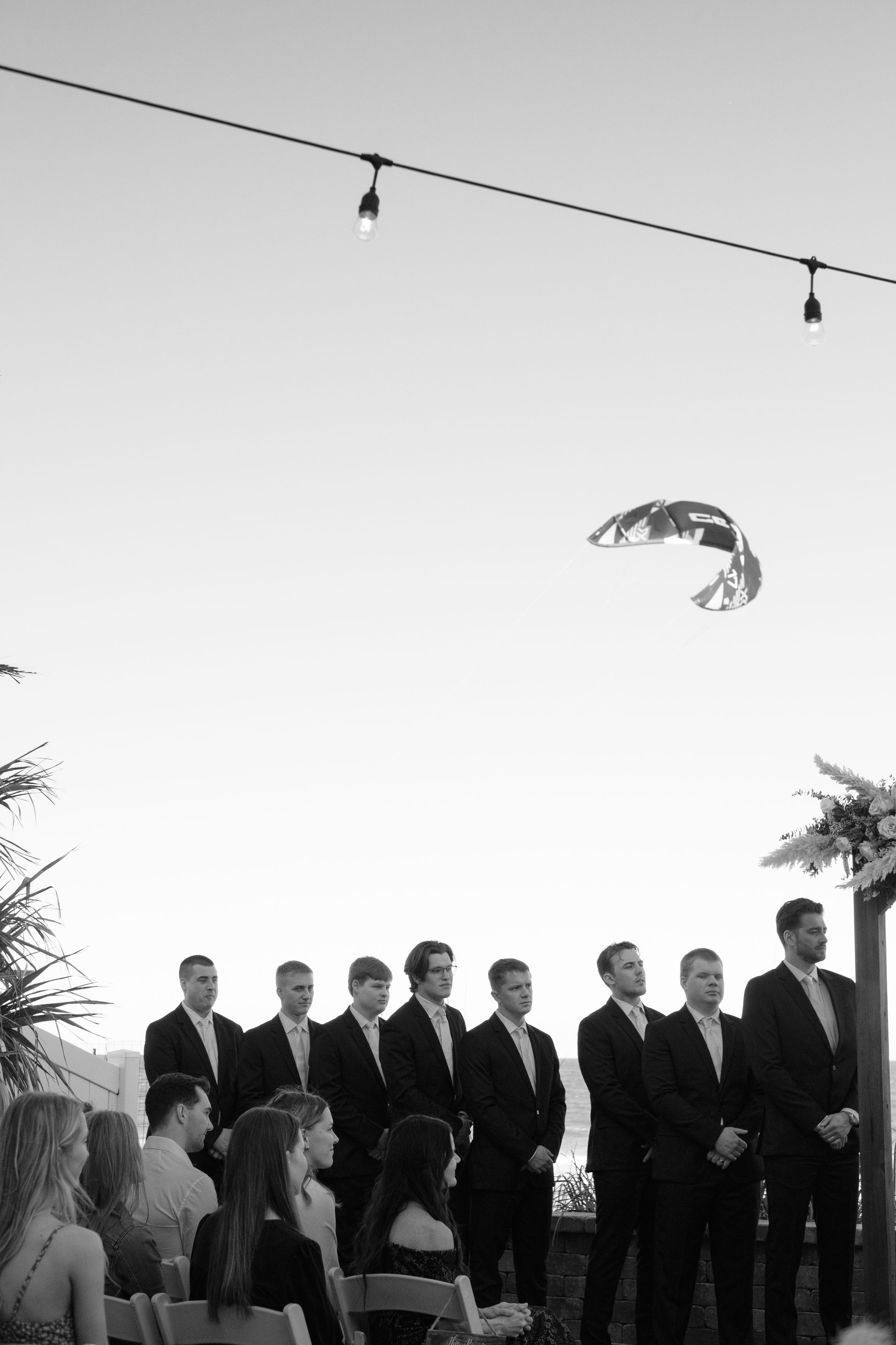 Candid shot of the groomsmen and someone parasailing behind them in black and white