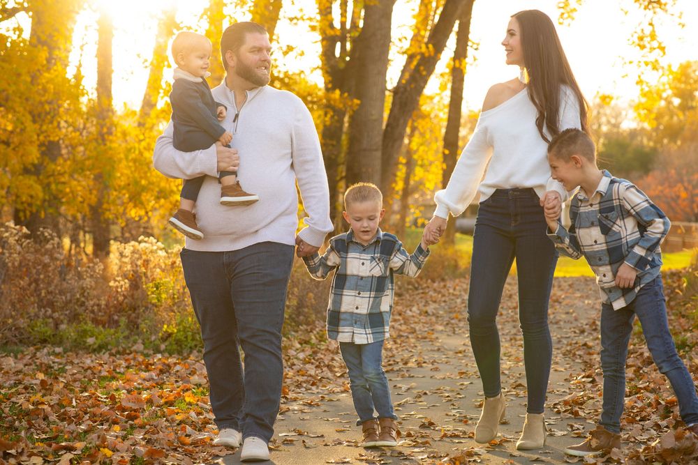 Photo of a family walking together with authentic emotion on autumn path through golden woods at sunset with fallen leaves on ground.