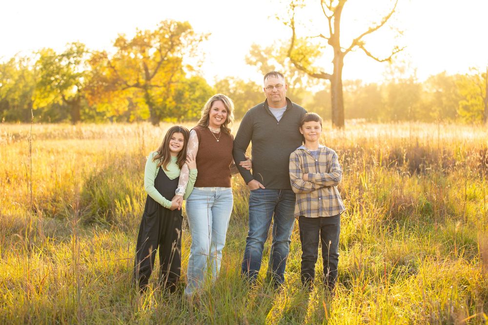 Golden and glowing family portrait of a family posing in a field of tall grasses.  Family photo was taken in South Dakota.