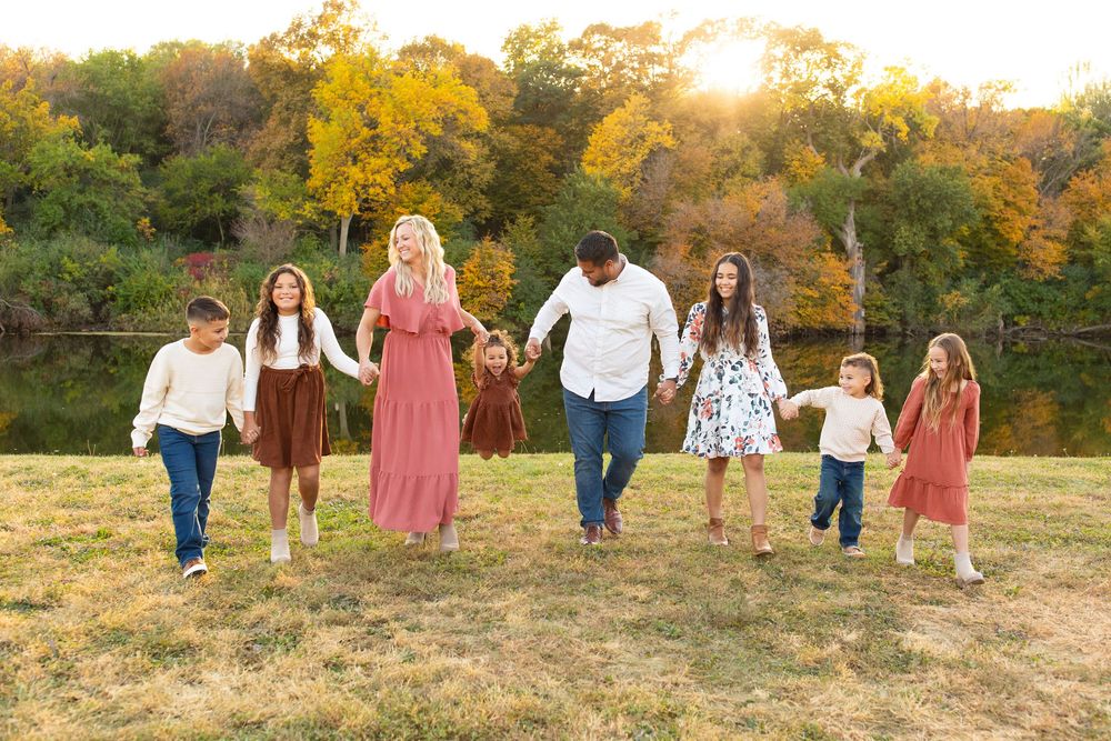 A family walks together through a golden autumn field at sunset, with water behind them creating a warm and joyful family portrait scene.