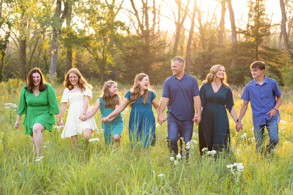 Iowa family photographer emotional candid image of a family holding hands and walking in a field of wild flowers at sunset.
