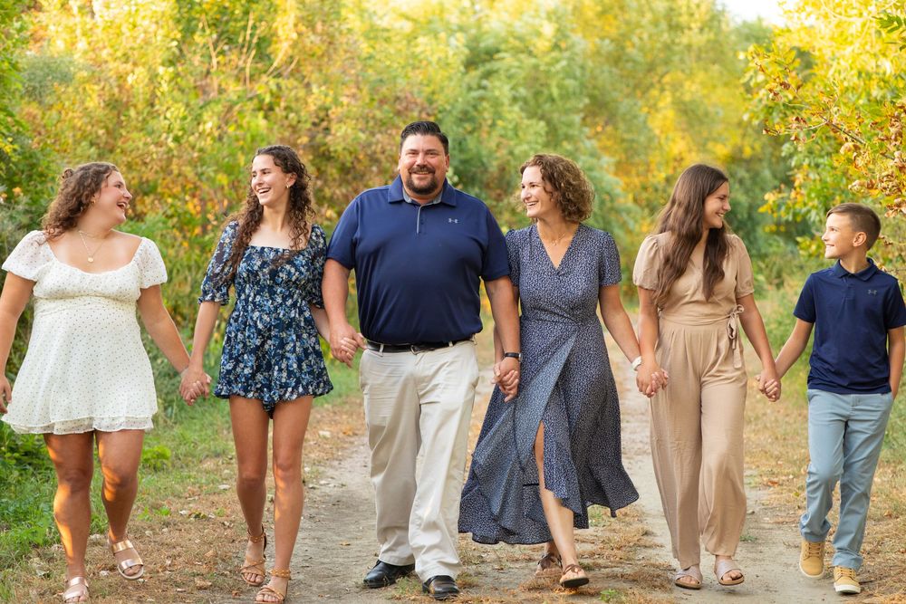 A family walks together on a path through golden autumn foliage during a sunny outdoor photo session at Ponca State Park in Nebraska.