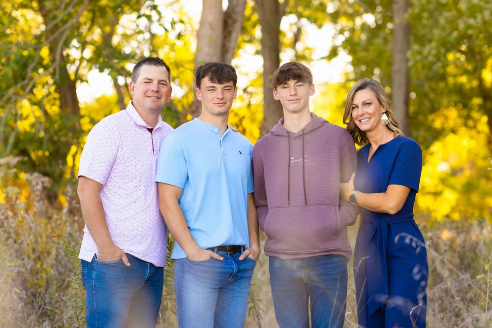 A family poses together outdoors at Homer Lake, IL during golden hour with trees and autumn foliage in the background.