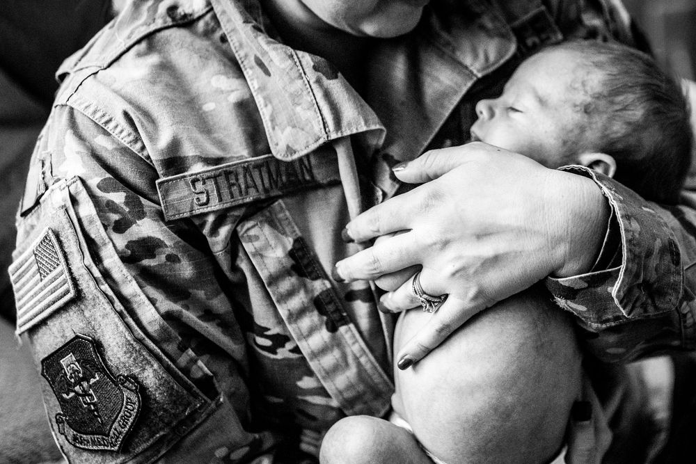 Military service member cradles her newborn in an emotional black and white moment showing raw and genuine connection.
