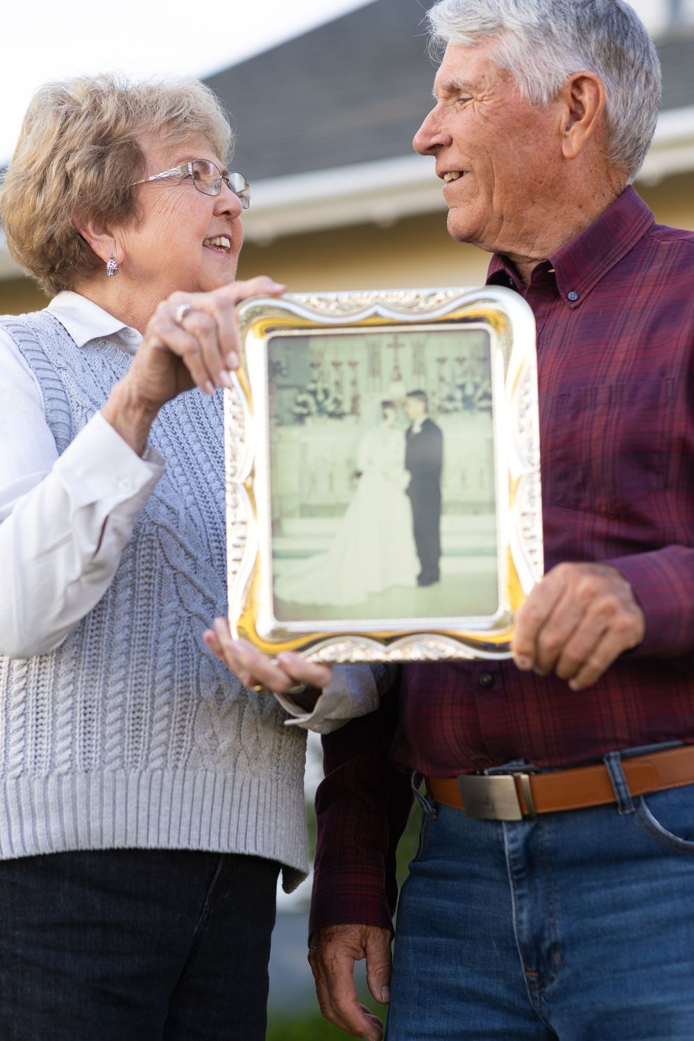 Senior couple sharing nostalgic moment while holding a vintage wedding photo in ornate frame.