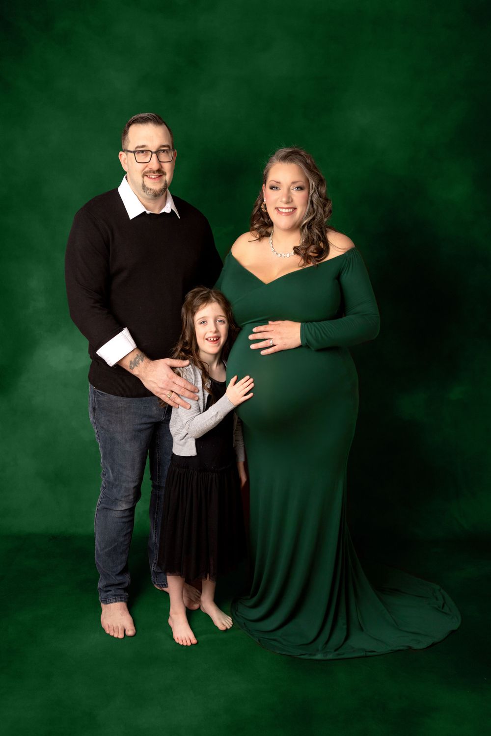 A family maternity portrait against a deep green backdrop. Photography Halifax
