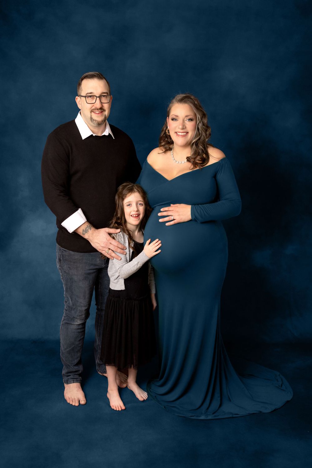 Expectant family poses against dark blue backdrop in formal maternity photo session. Photography Halifax