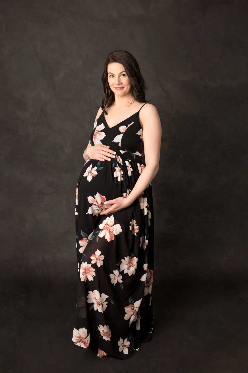 Maternity photo of woman in black floral maxi dress against dark background. Maternity Photography Halifax