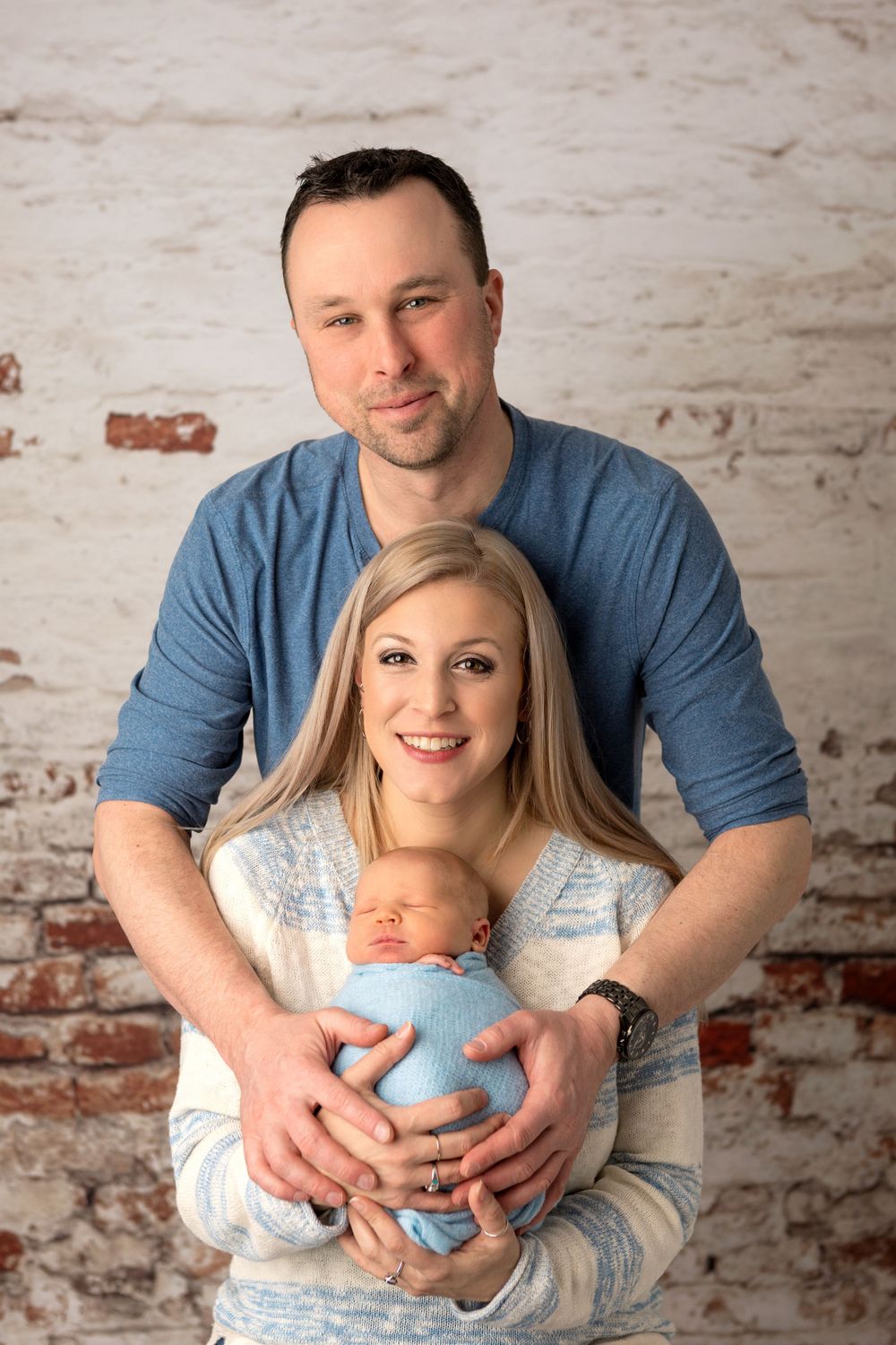New parents cradle newborn baby against rustic brick wall background. Newborn & Family Photography Halifax
