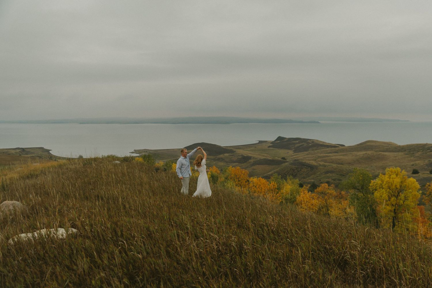 Rolling hills and autumn trees stretch across a vast landscape under moody skies.