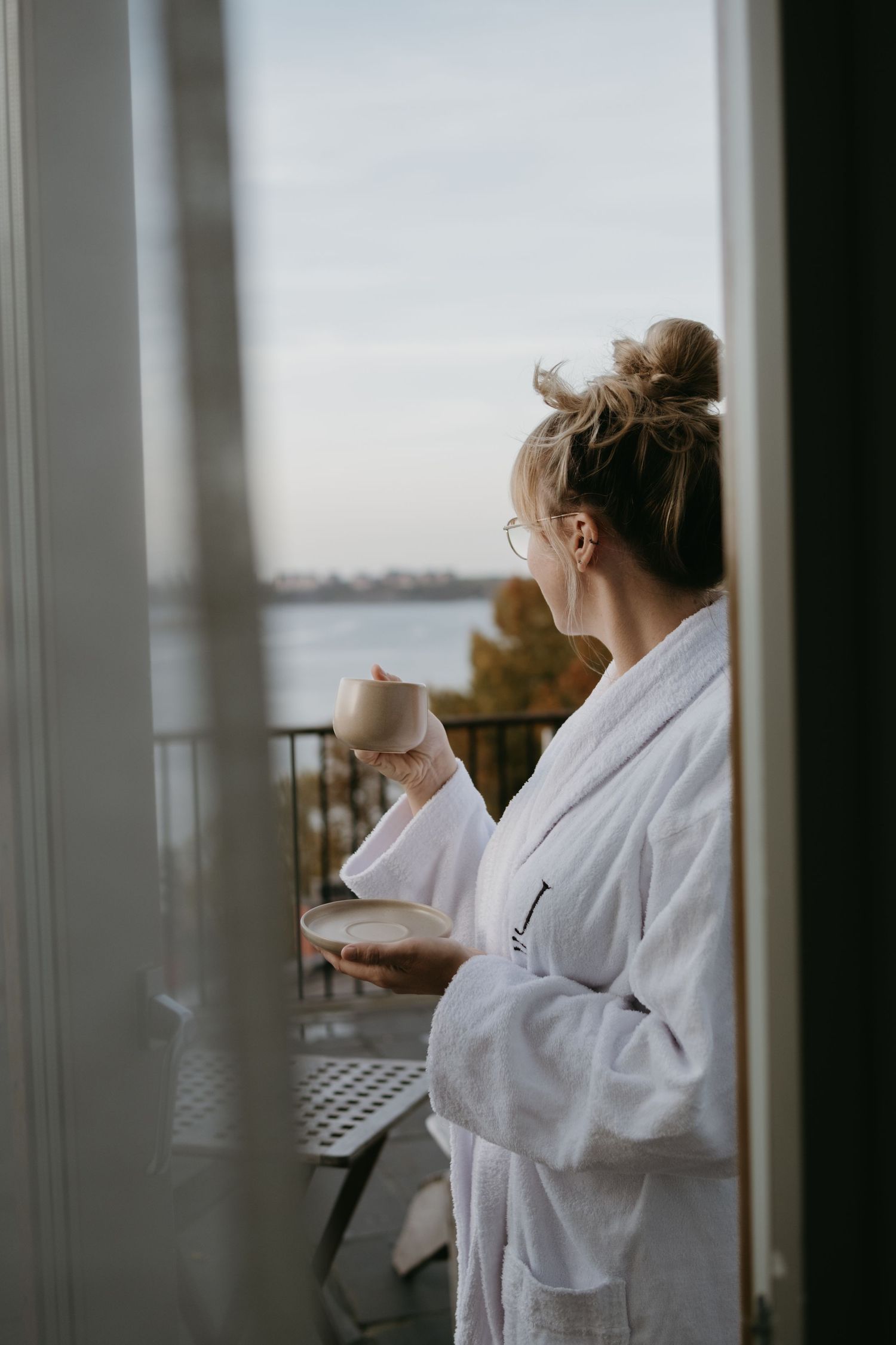 woman holding a cup of coffee, standing on a hotel balcony looking at view while being captured by hotel photographer in Stockholm
